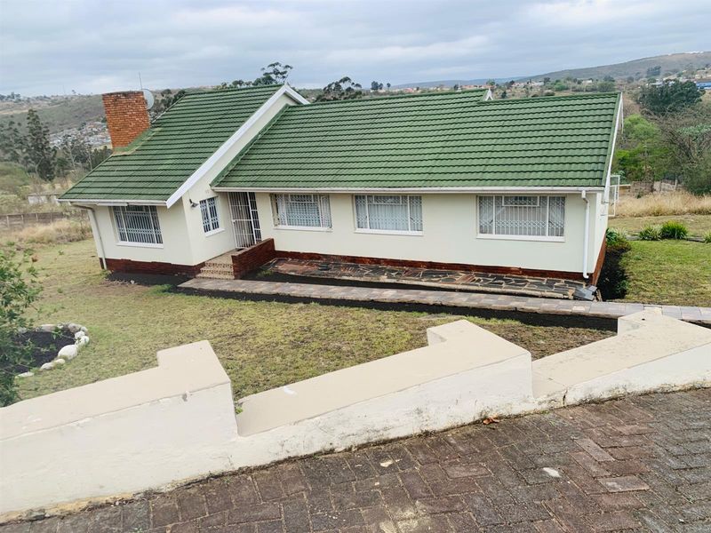 A detached single-story house featuring a green tiled roof, brick chimney, and security bars on windows, set within a spacious garden plot.