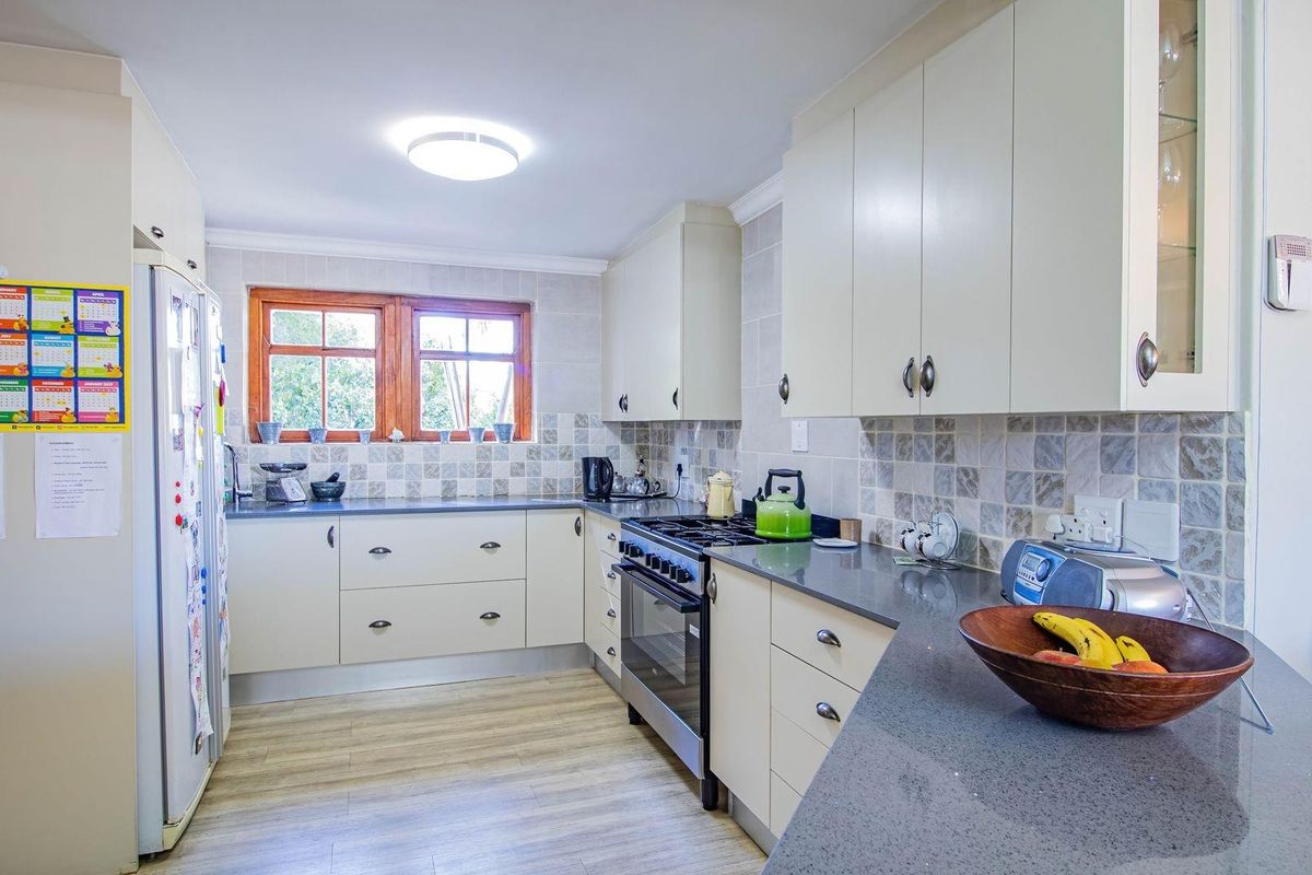 A functional kitchen featuring light-toned cabinetry, stone-look countertops, tiled backsplash, and a freestanding oven with extractor fan.
