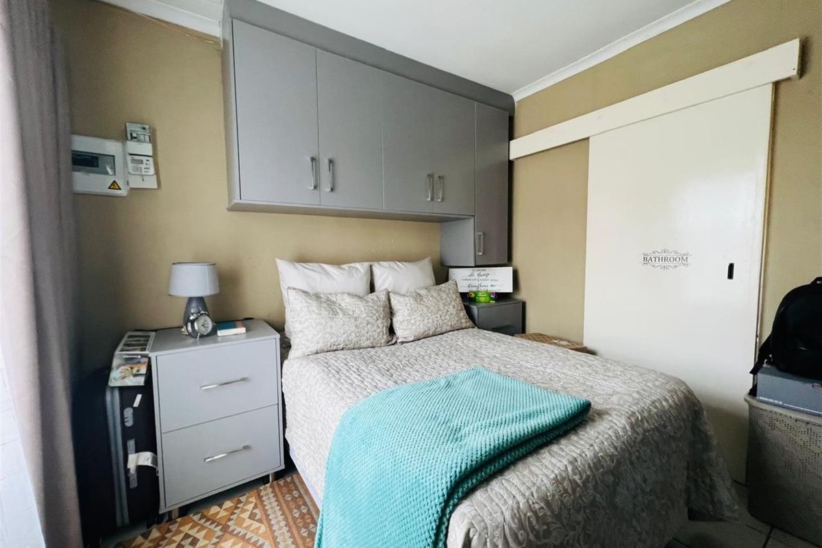 A compact bedroom featuring built-in overhead cabinetry and a sliding door providing direct access to an en-suite bathroom.
