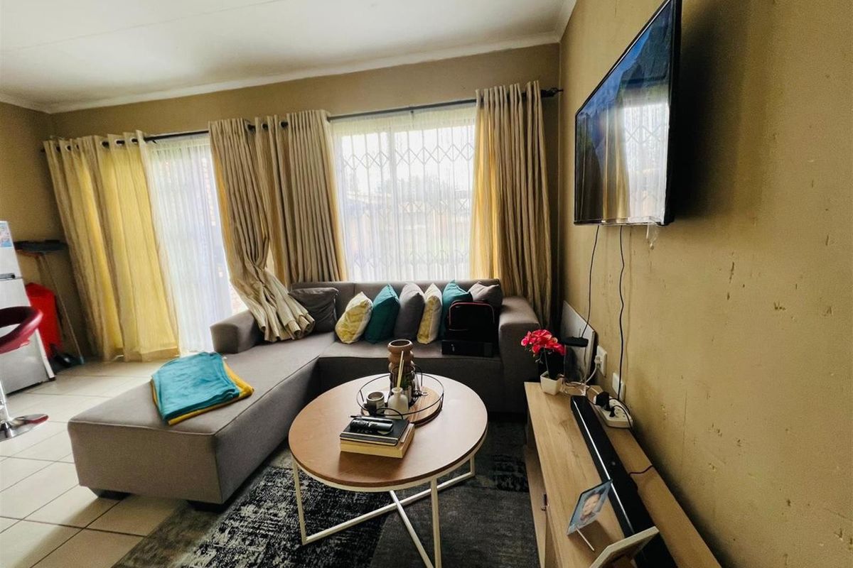 A cozy living room featuring tiled flooring, large windows with security gates, and wall-mounted television space.