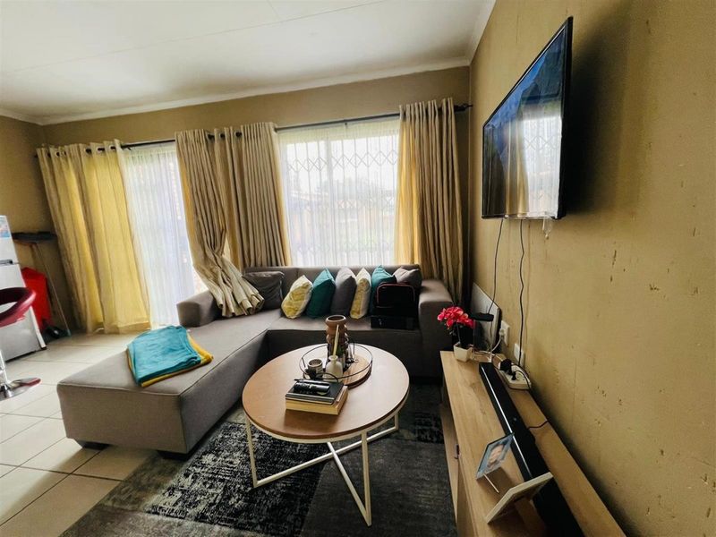 A cozy living room featuring tiled flooring, large windows with security gates, and wall-mounted television space.