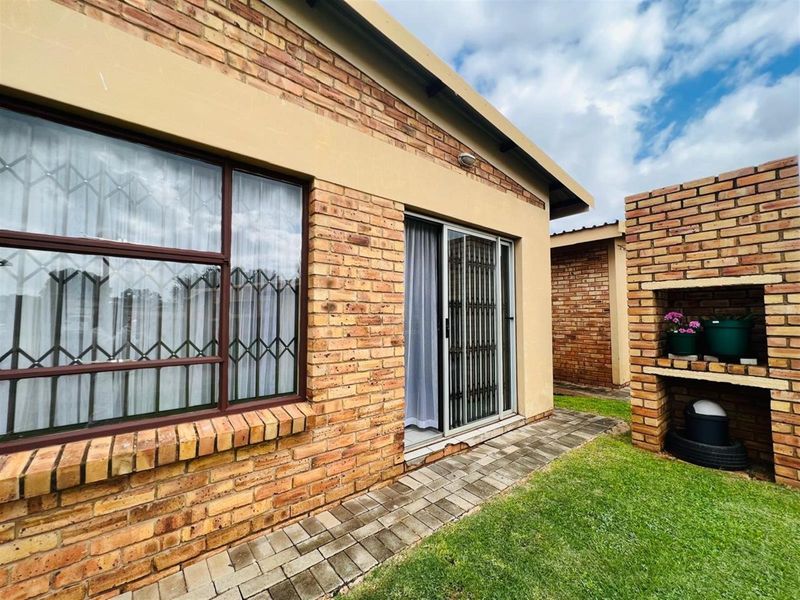 Exterior view of the apartment featuring face brick walls, a paved walkway, and a built-in brick braai area in the garden.