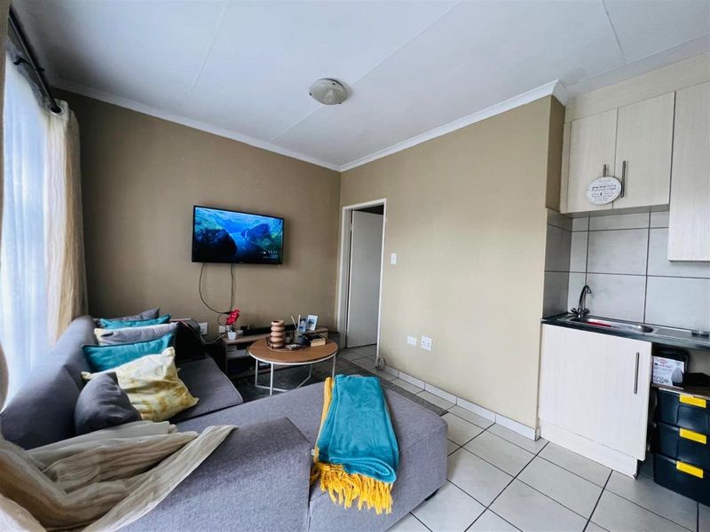 Compact open-plan living area featuring a kitchenette with built-in cabinetry, tiled flooring, and direct access to adjacent rooms.