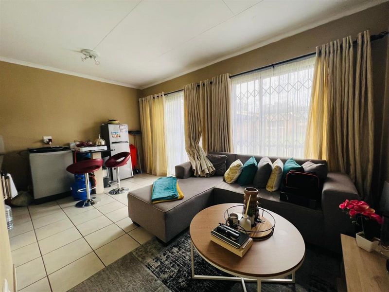 Open plan living area featuring tiled flooring, large windows with curtain treatments, and a compact kitchenette corner.