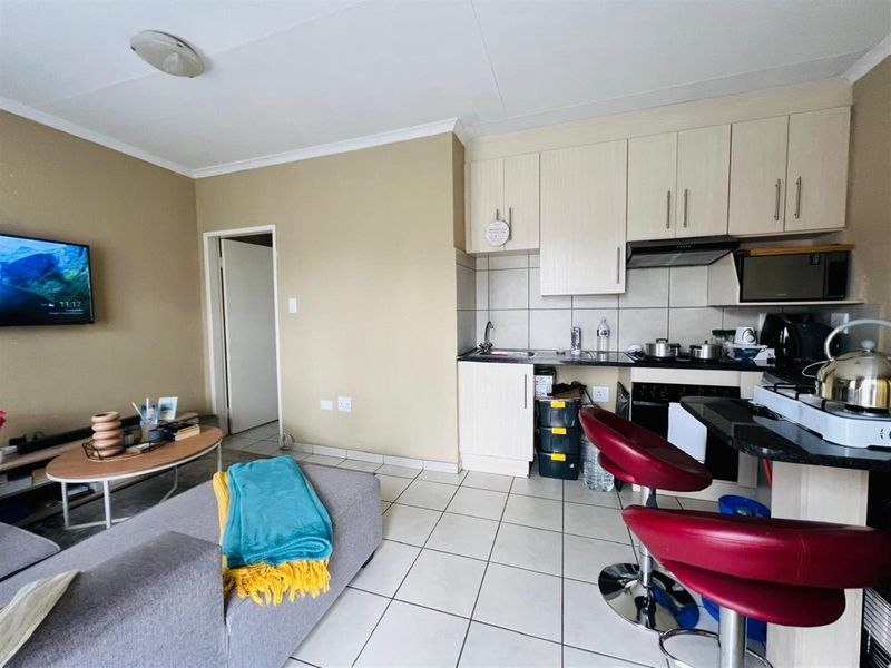 Open-plan living area featuring a compact kitchen with built-in cabinetry, tiled flooring, and a breakfast bar, seamlessly connecting to the lounge space.