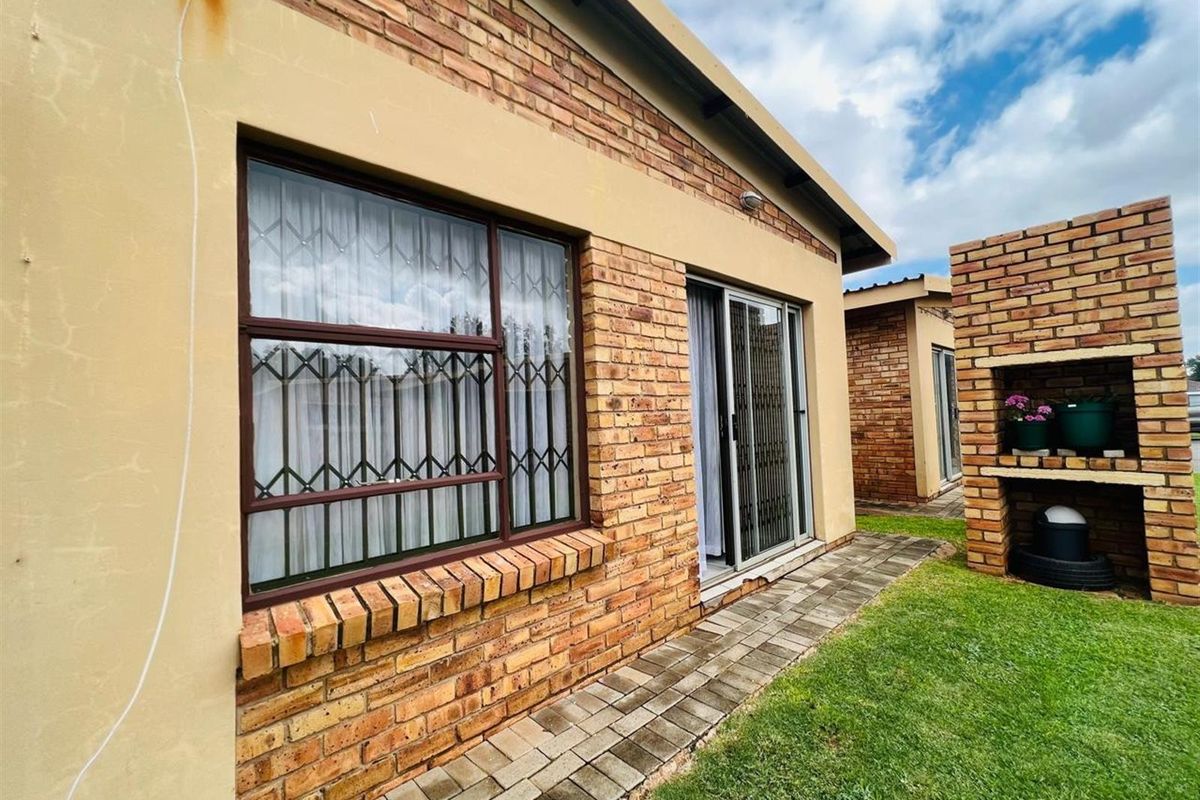 Exterior view of the apartment featuring face-brick facade, sliding glass doors, security bars on windows, and a built-in brick braai area in the garden.