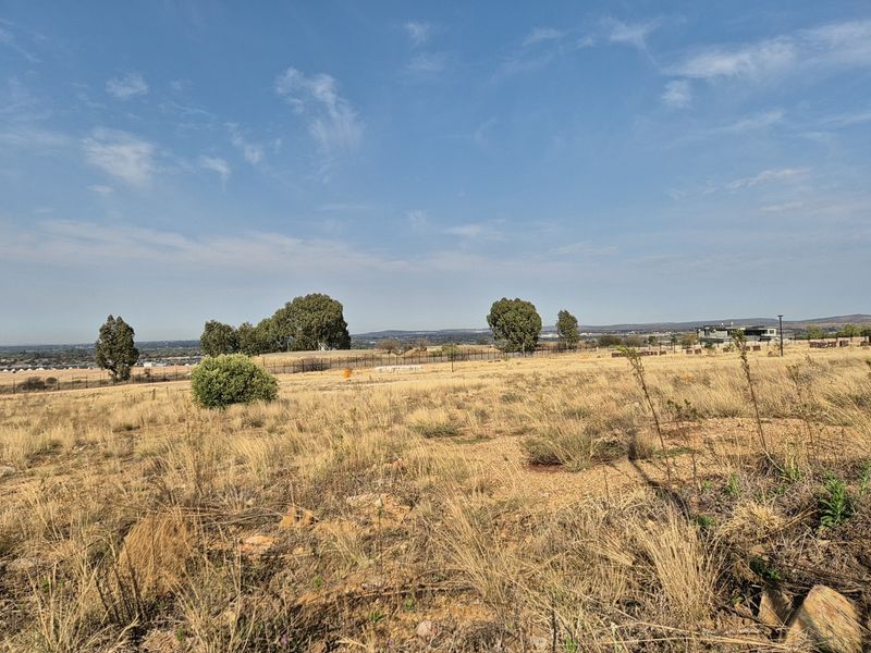 A wide-angle view of the vacant residential land, showcasing the natural landscape, dry grass, and surrounding estate perimeter fencing.