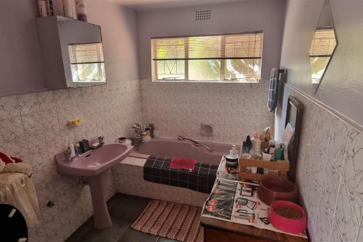 A dated bathroom featuring a purple pedestal sink, a built-in bathtub, and partial wall tiling, offering a functional space ready for modernization.