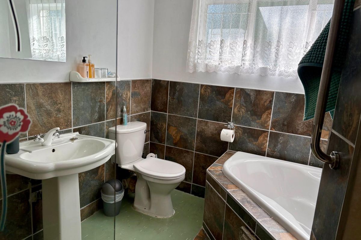 A functional bathroom featuring a pedestal basin, toilet, and a built-in bathtub with dark stone-effect wall tiling.