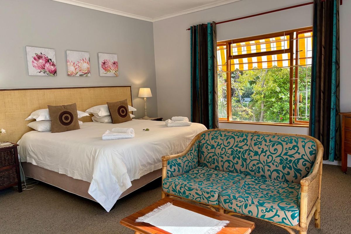 A comfortable bedroom featuring a large window with garden views, neutral wall tones, and carpeted flooring.