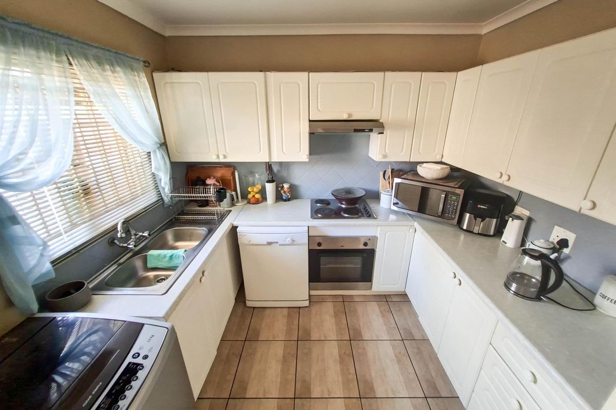 A functional kitchen featuring white cabinetry, built-in oven, electric hob, extractor fan, and a double stainless steel sink with tiled splashbacks.