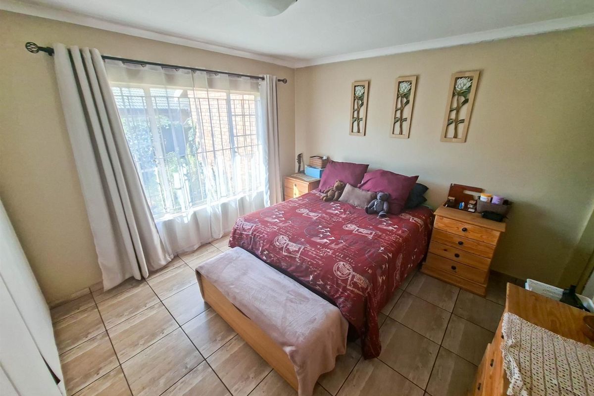 A bedroom featuring tiled flooring, a large window with security bars, and built-in cupboard space.