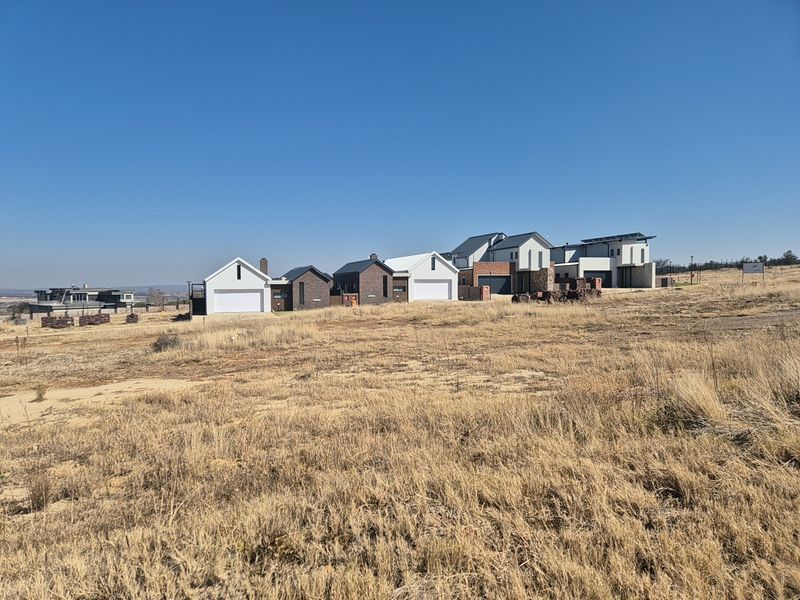 A wide-angle view of a vacant residential plot with established modern homes visible in the background.