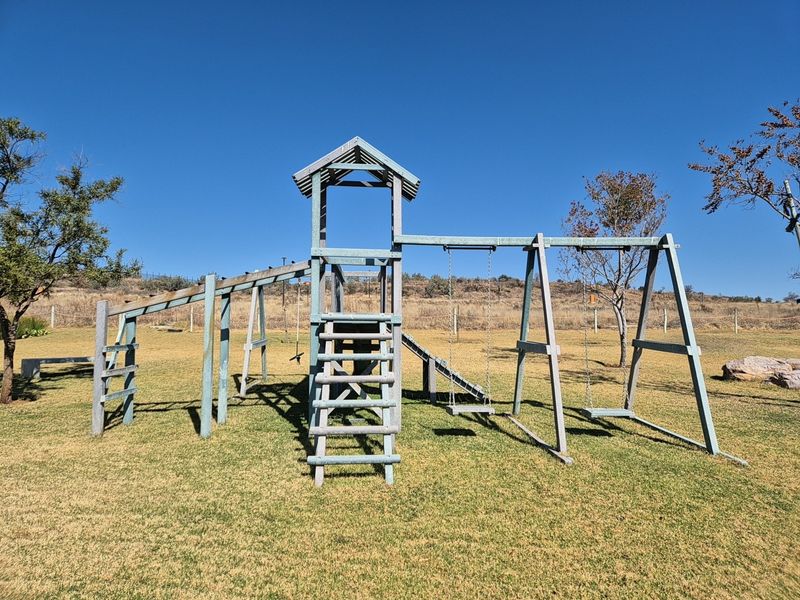 A well-maintained residential garden featuring a wooden jungle gym with swings and a slide set on a grassy lawn.