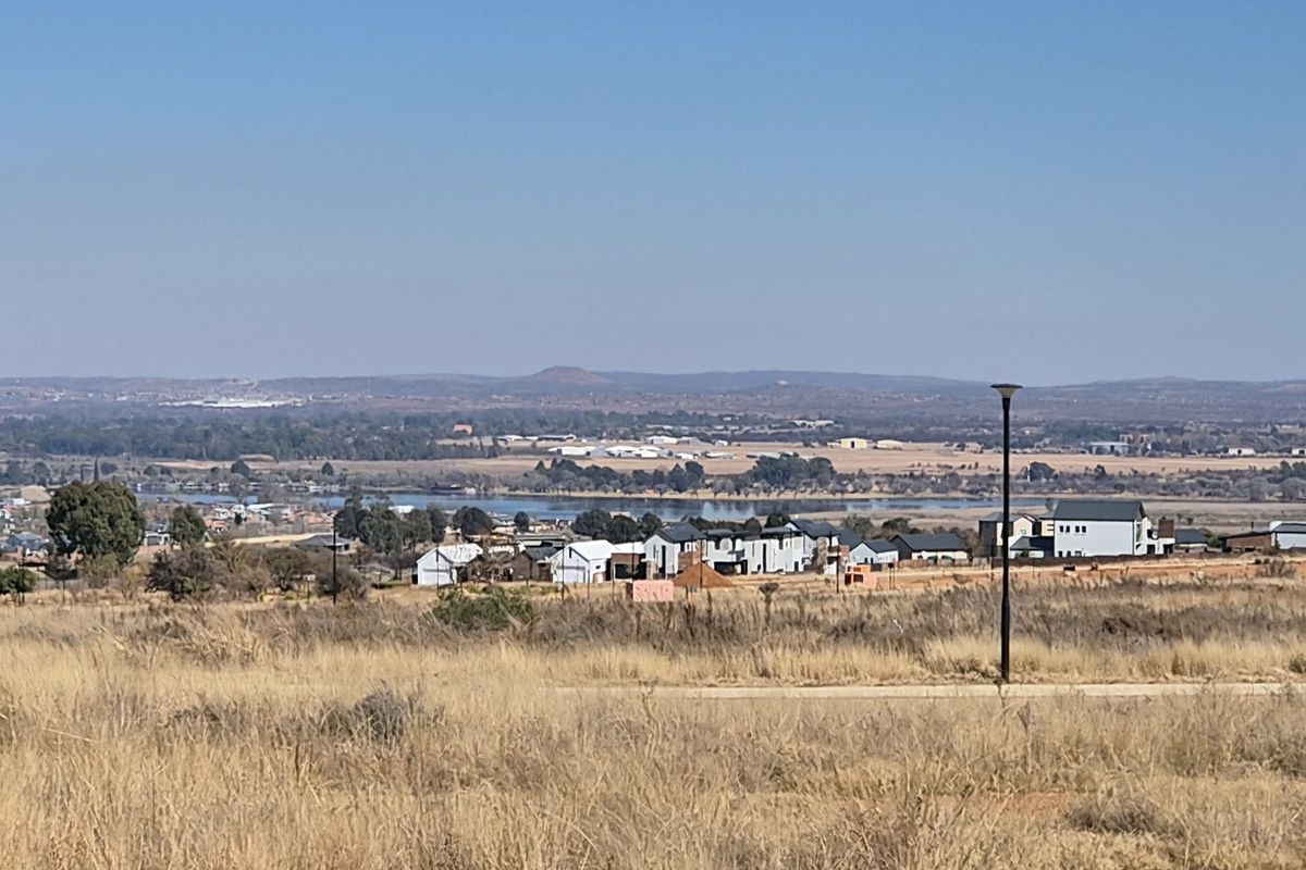 A wide-angle view of the surrounding landscape, featuring open fields, distant residential developments, and a scenic water body under a clear sky.