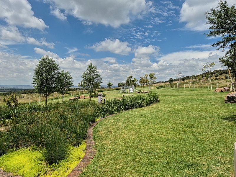 A well-maintained, expansive residential garden featuring manicured lawns, structured garden beds with brick edging, and scenic open views.