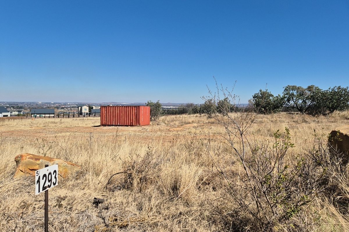 A view of a vacant residential plot featuring dry grass, natural terrain, and a property boundary marker.