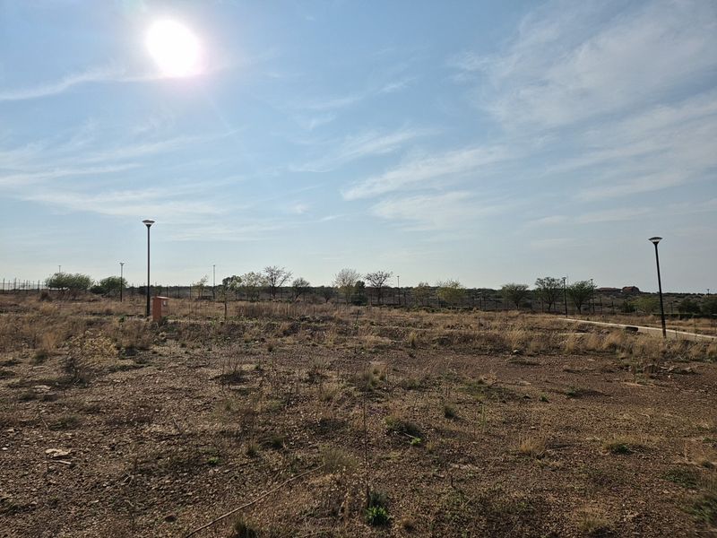 A vacant residential plot featuring established street lighting, perimeter fencing, and utility connection points, ready for development.