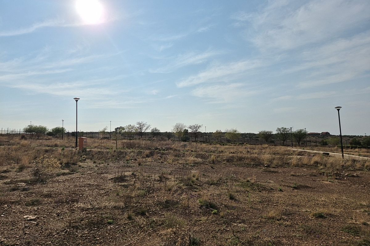 A vacant residential plot featuring established street lighting, perimeter fencing, and utility connection points, ready for development.