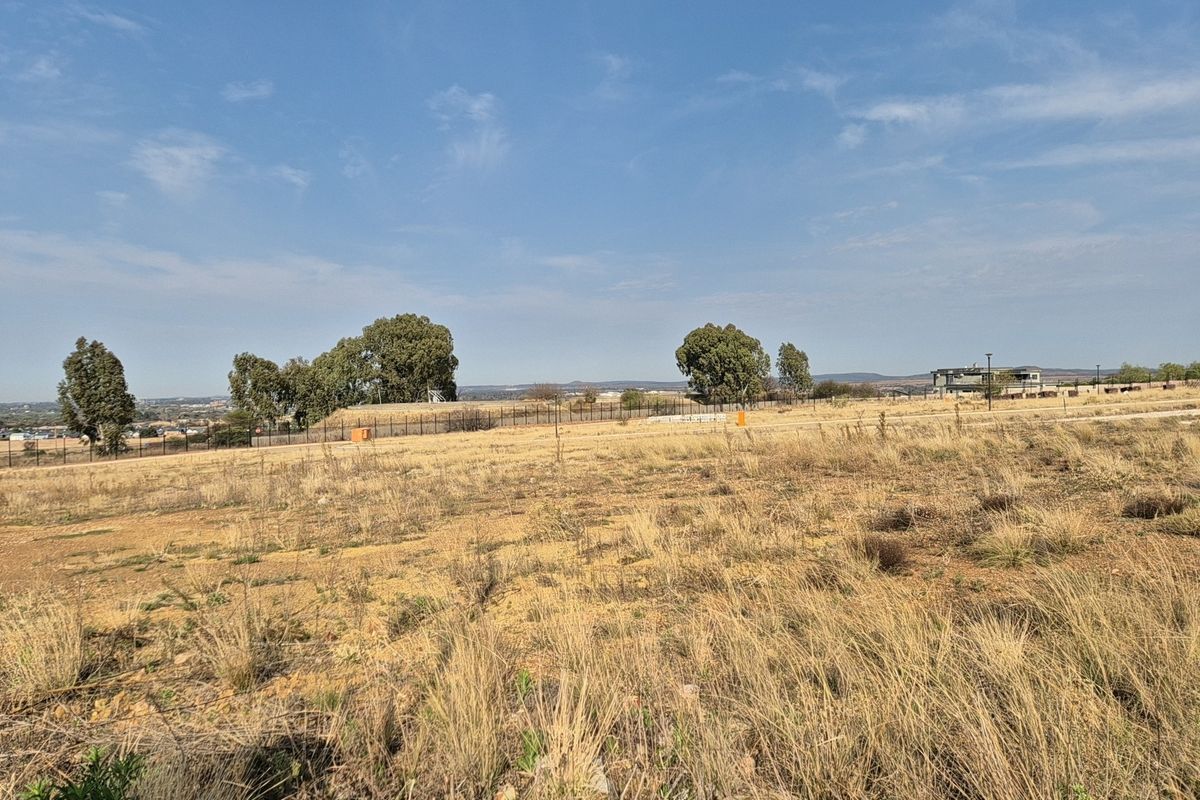 A view of a vacant residential plot featuring dry grass, perimeter fencing, and distant landscape views.