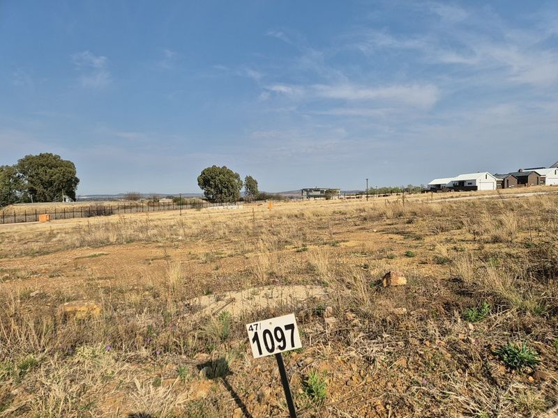 A view of a vacant residential plot featuring natural vegetation and boundary fencing, ready for development in a residential estate.