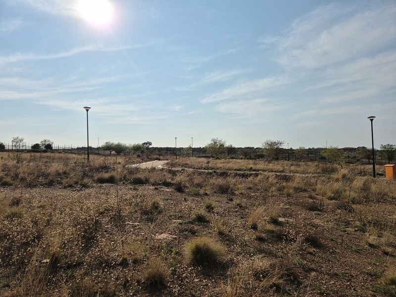 A view of a vacant residential plot featuring established perimeter fencing, street lighting, and a paved access path.