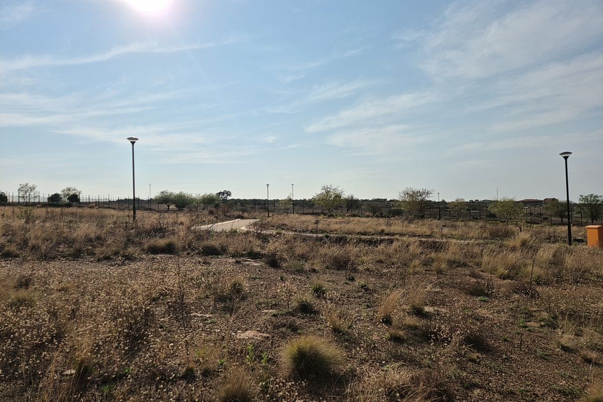 A view of a vacant residential plot featuring established perimeter fencing, street lighting, and a paved access path.