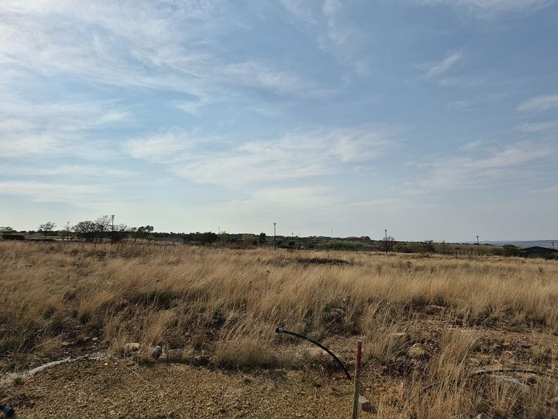 A view of a vacant residential plot featuring dry grass and visible utility connection points, ready for future development.
