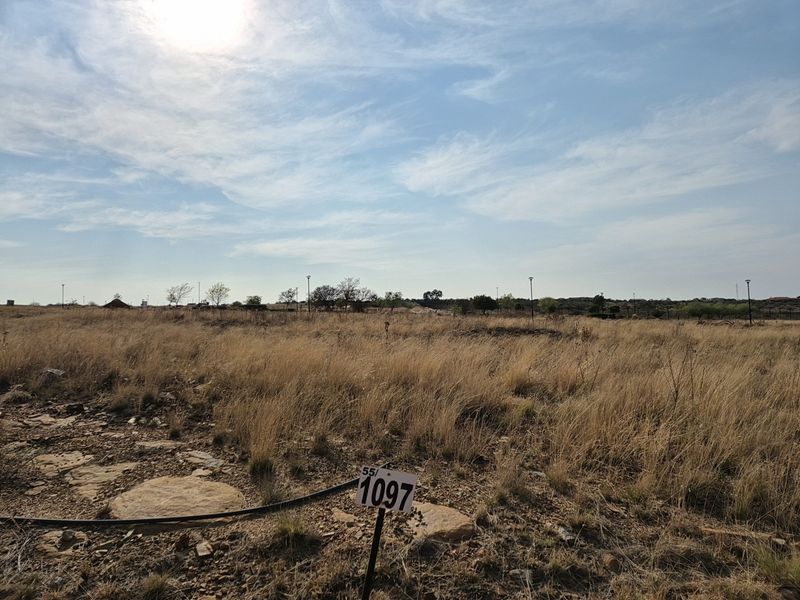 A view of a vacant residential plot featuring natural dry grass and a clear boundary marker, ready for development.