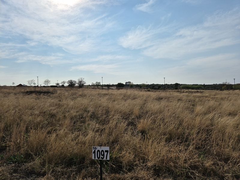 A vacant residential plot of land featuring dry grass, boundary fencing, and street lighting, ready for development.