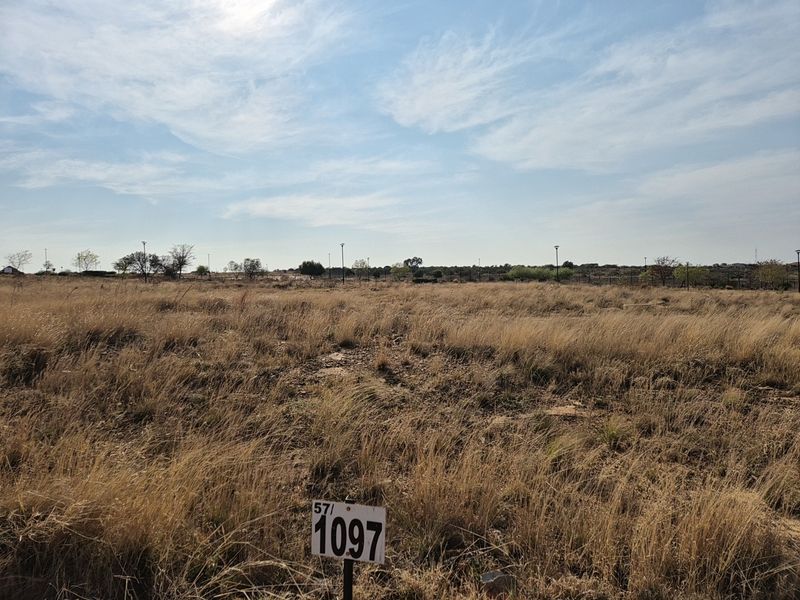 A vacant residential plot of land featuring dry grass, boundary fencing, and street lighting, ready for development.