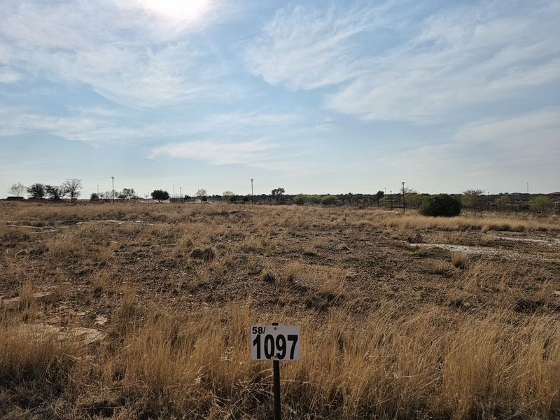 A view of a vacant residential plot of land featuring natural dry grass and a clear boundary marker.