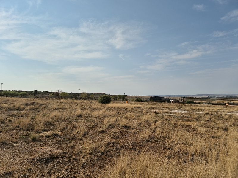 A wide-angle view of the vacant residential land, showcasing the natural landscape, surrounding terrain, and distant neighborhood infrastructure.