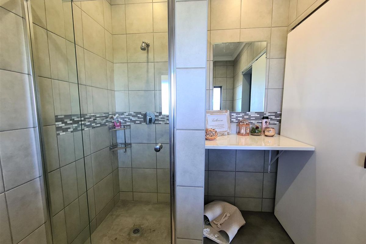 A functional bathroom featuring a glass-enclosed shower with tiled walls and a vanity area with a wall-mounted mirror.