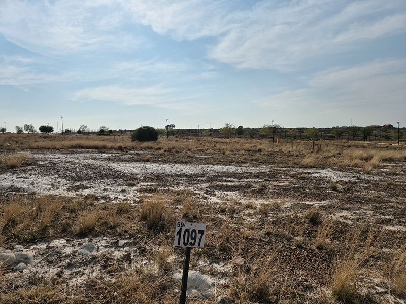 A vacant residential plot of land featuring natural vegetation and a clear plot marker, ready for development.