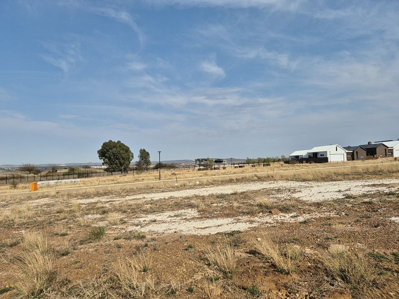 A vacant residential plot featuring natural terrain, perimeter fencing, and surrounding neighborhood views, ready for development.