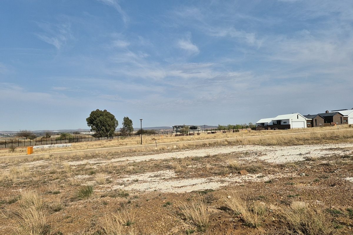 A vacant residential plot featuring natural terrain, perimeter fencing, and surrounding neighborhood views, ready for development.
