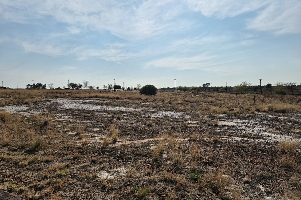 A wide-angle view of a vacant residential plot featuring natural dry vegetation, perimeter fencing, and installed outdoor lighting poles.