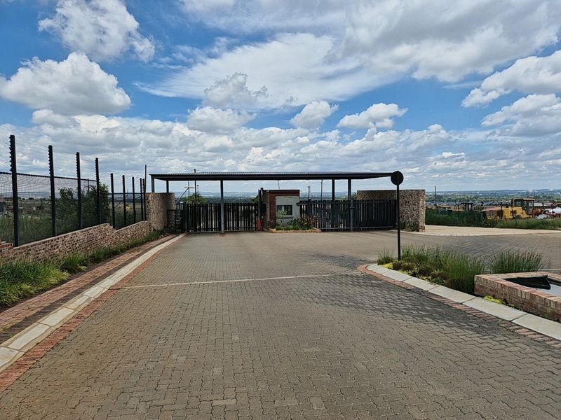 A secure gated entrance to the residential estate featuring a guard house, paved driveway, and perimeter electric fencing.