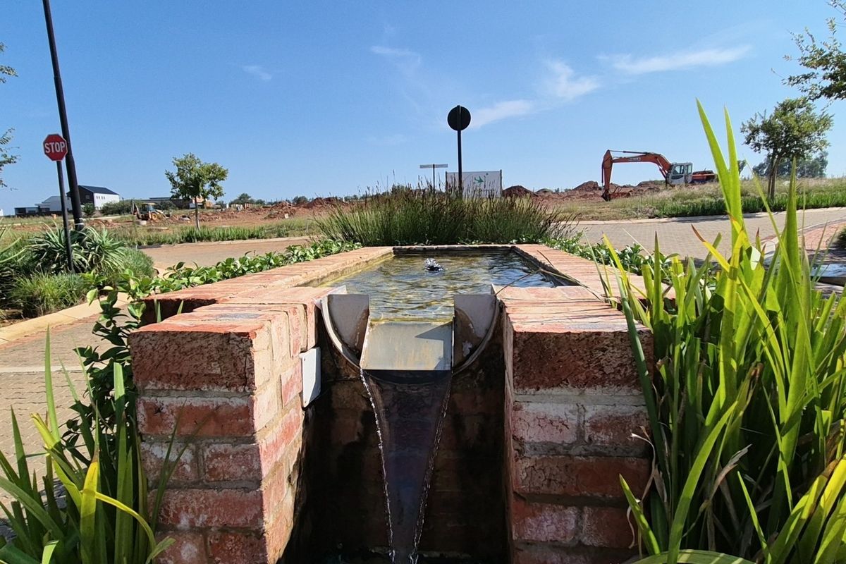 A decorative brick water feature set within a landscaped garden area, showcasing established greenery and paved pathways in a residential development setting.