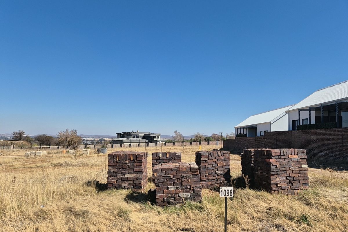 A vacant residential plot featuring dry grass, a boundary wall, and a plot marker, situated in a developed residential estate.