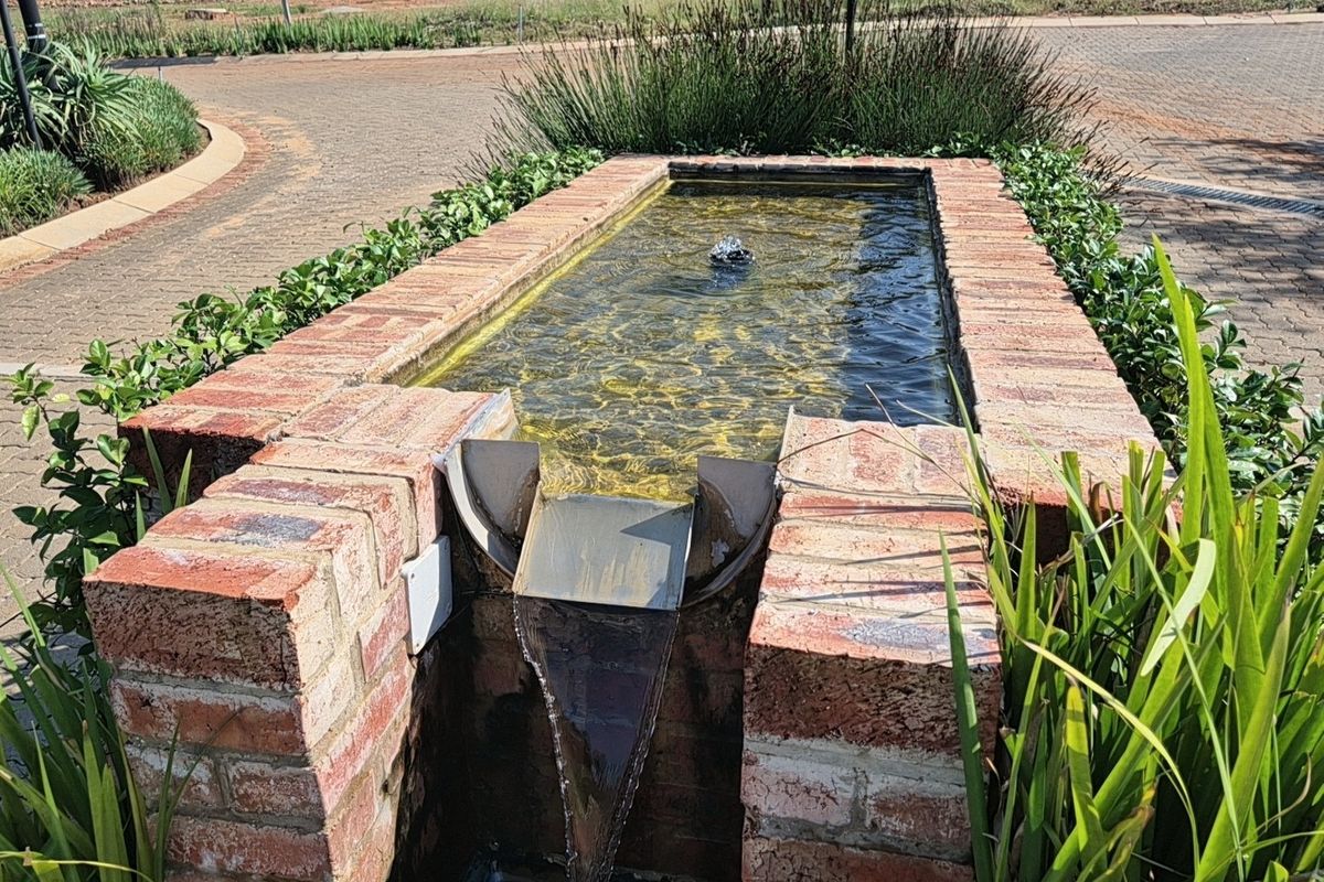 A well-maintained brick water feature and fountain located within a landscaped garden area on a residential property.