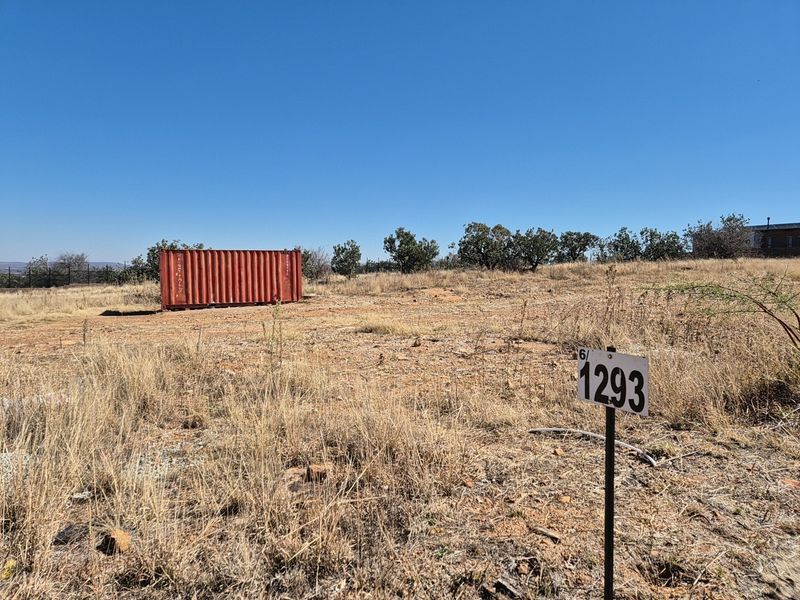 A view of a vacant residential plot featuring dry grass, boundary fencing, and a storage container on site.