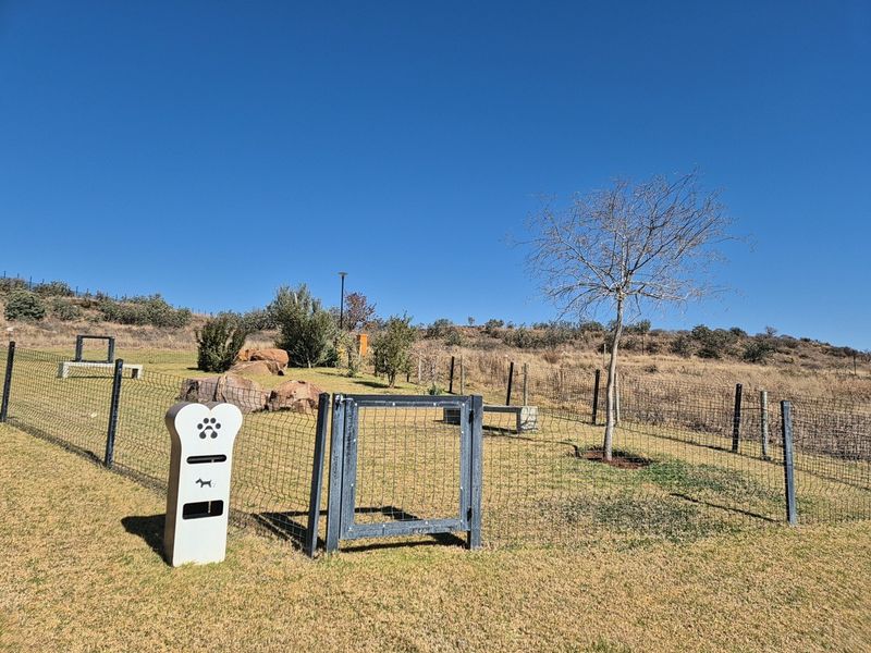 A well-maintained outdoor garden area featuring wire mesh fencing, a secure metal gate, and a dedicated pet waste disposal station.