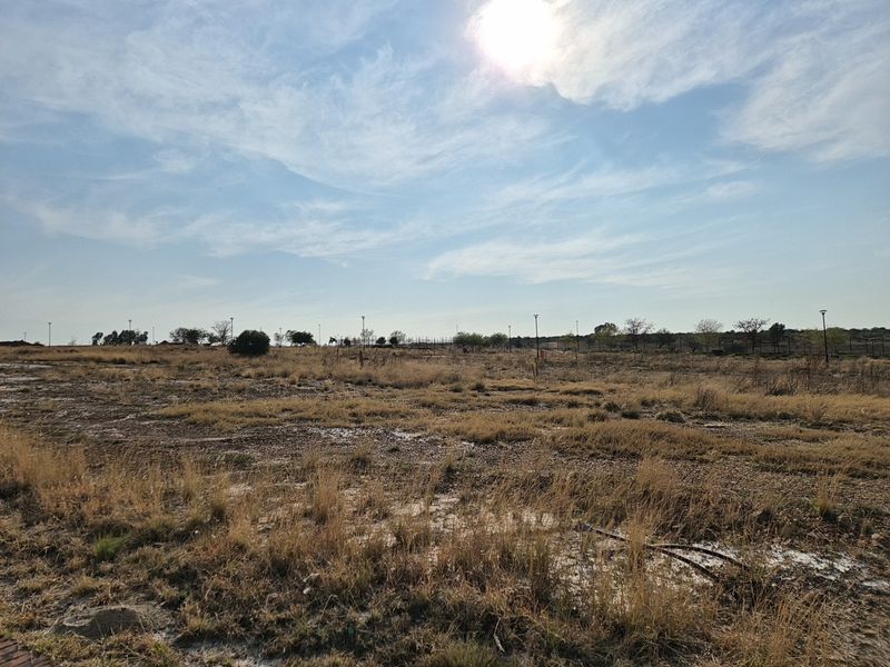A wide-angle view of a vacant residential plot featuring dry grass and open land, suitable for future development.