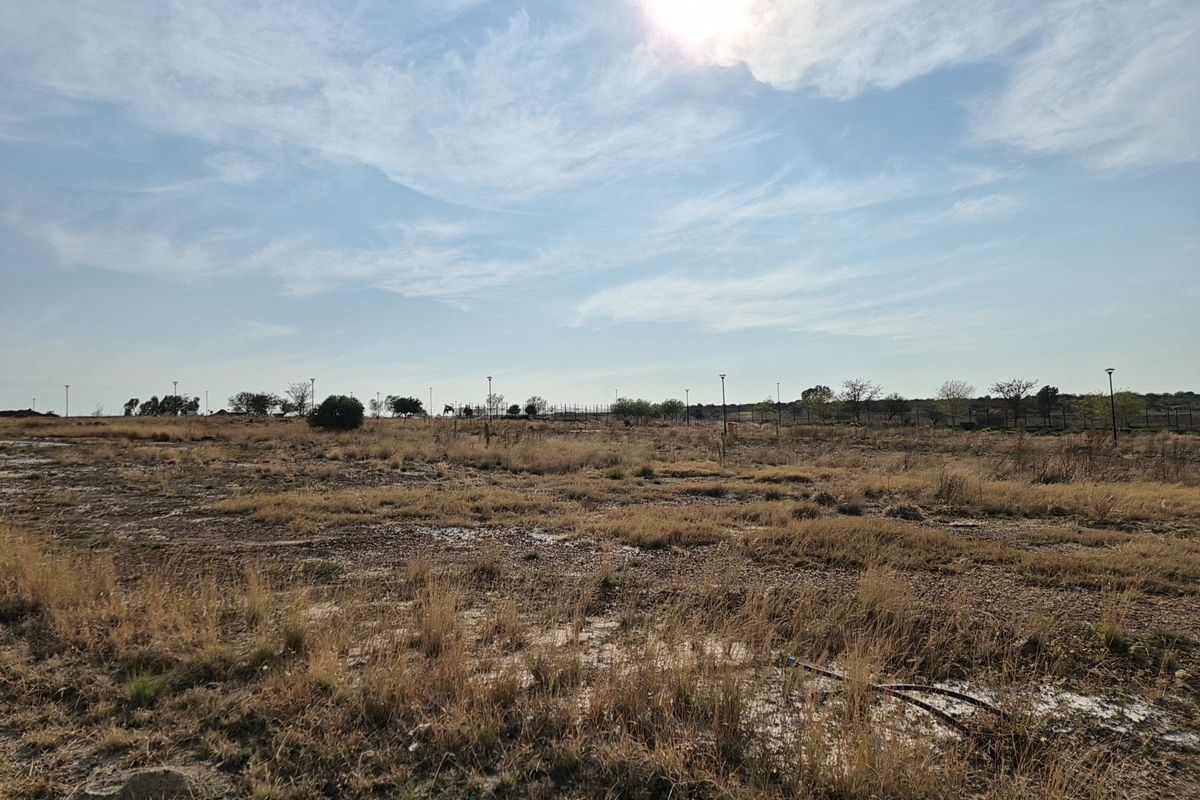 A wide-angle view of a vacant residential plot featuring dry grass and open land, suitable for future development.