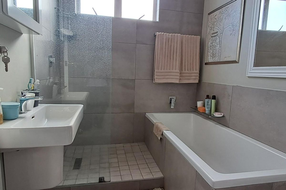 A modern bathroom featuring a wall-mounted basin, a built-in bathtub, and a glass-enclosed shower area with neutral wall tiling.