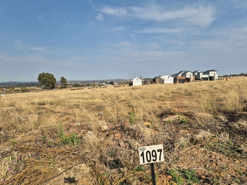 A view of a vacant residential plot featuring natural dry grass and a clear plot number marker, situated in a developing estate.