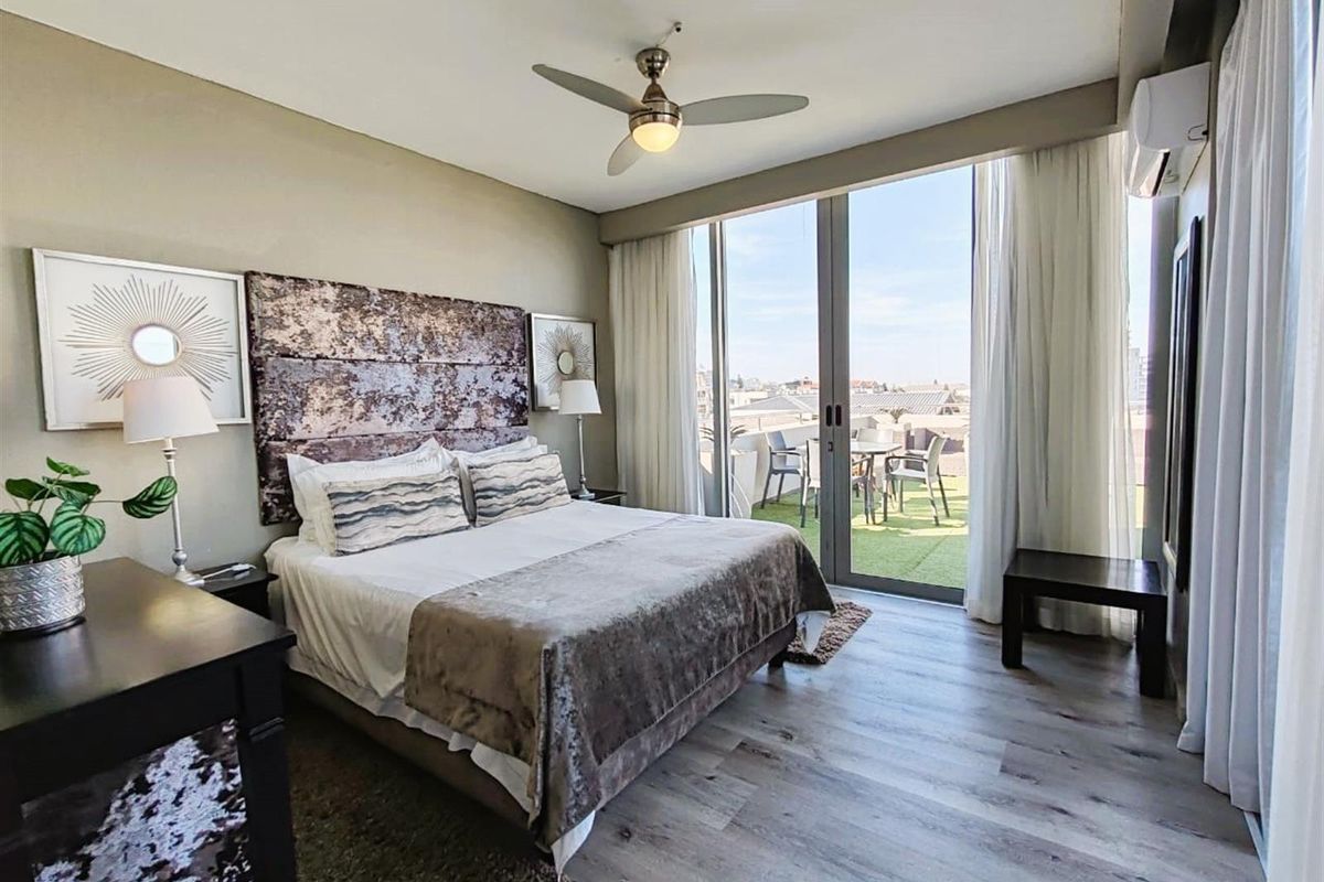 Spacious bedroom featuring wood-look flooring, a ceiling fan, and large sliding glass doors opening onto a private balcony with outdoor views.