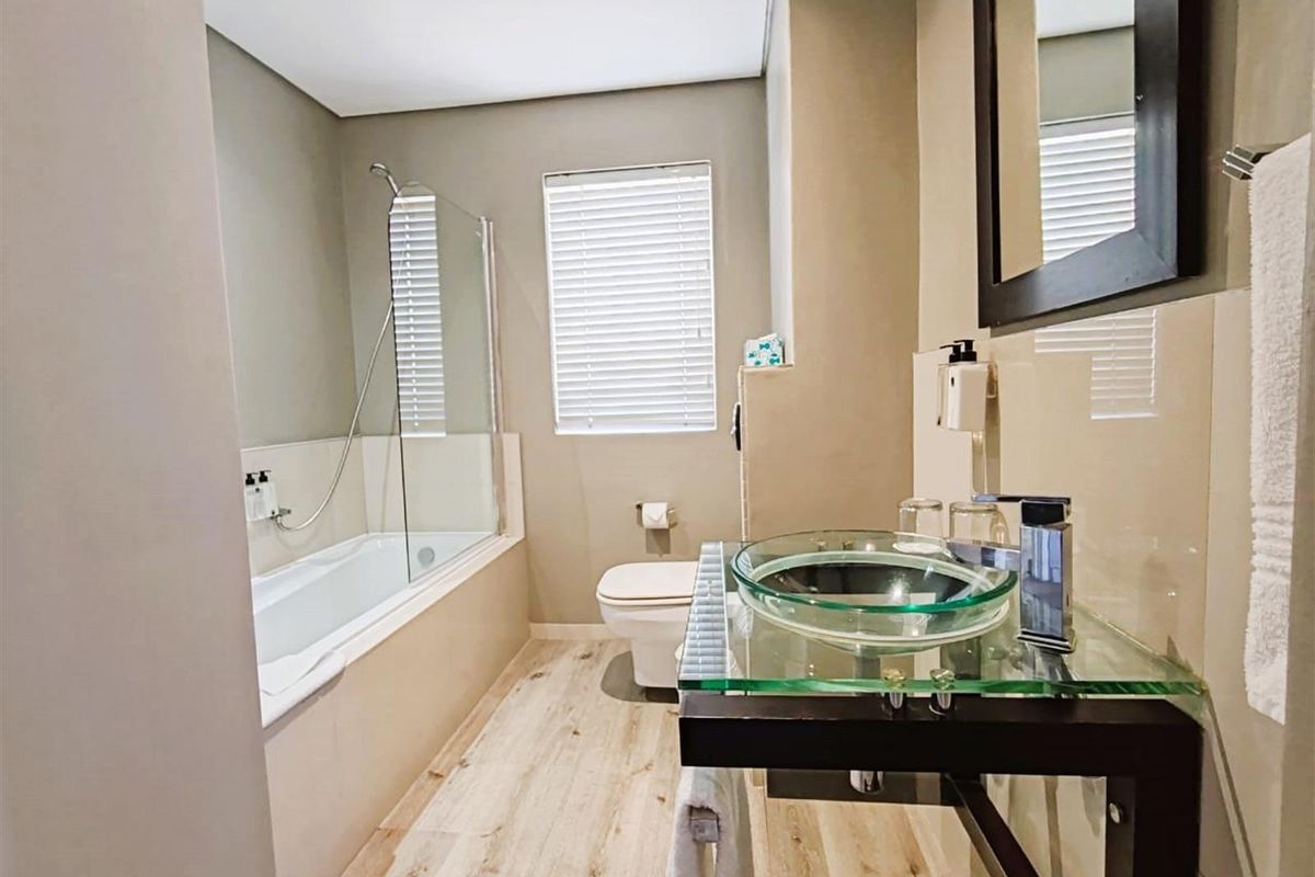 Modern bathroom featuring a glass vessel sink, a bathtub with a glass shower screen, and light wood-look flooring.